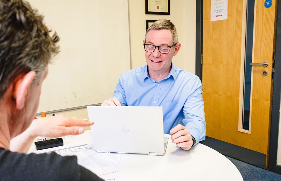 Rupert smiles looking over laptop in meeting