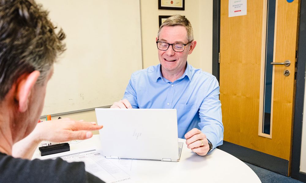 Rupert smiles looking over laptop in meeting